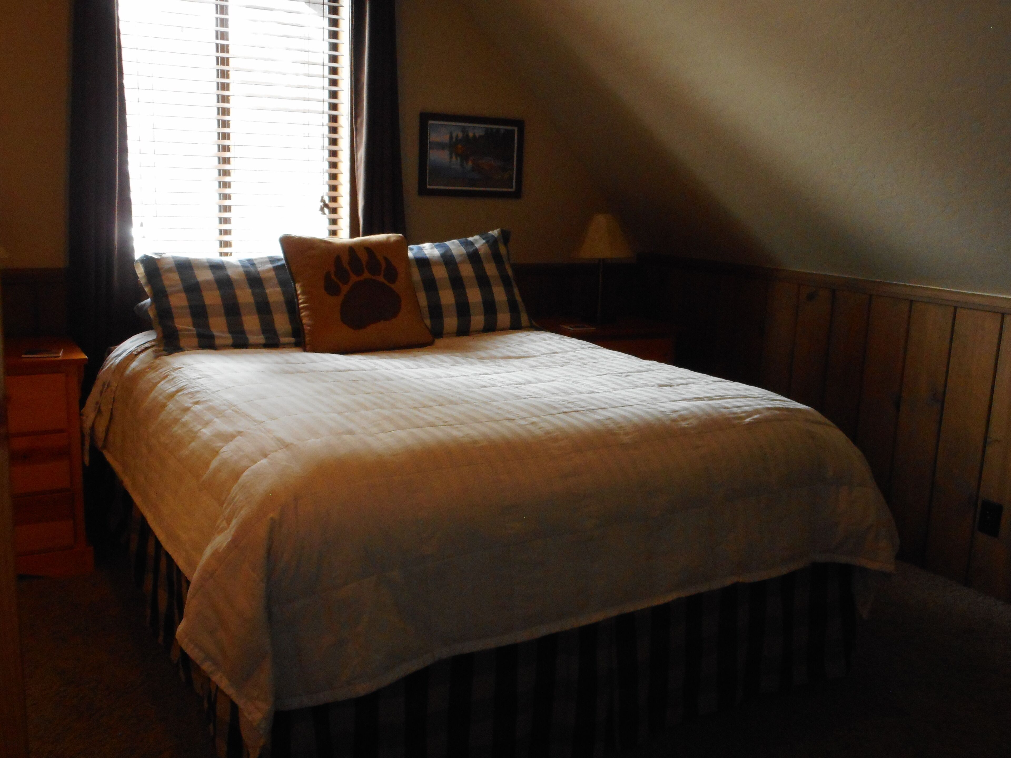 Ein ordentlich bezogenes Bett mit einer gesteppten Decke und einem Kissen mit Pfotenabdruck, flankiert von gestreiften Kissen.
