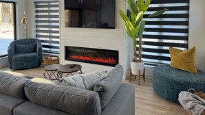 A modern living room with a fireplace, large windows, and comfortable seating. - Modern Riding Mountain Retreat (Onanole)
