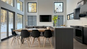 A modern kitchen with a central island, large windows, and a dining area with black chairs. - Modern Riding Mountain Retreat (Onanole)