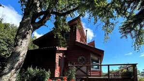 Una casa de madera roja con balcón, rodeada de un jardín bien cuidado con diversas plantas y flores.