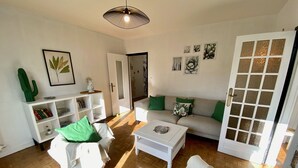 Un salon avec un canapé, une table basse et une bibliothèque. On y trouve une porte avec des panneaux de verre et une décoration en forme de cactus.