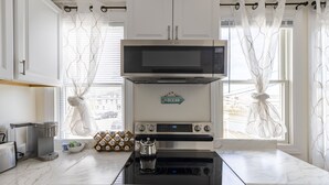 A modern kitchen with a built-in microwave, oven, and stovetop. There is a coffee maker, a kettle, and a set of coffee pods on the counter.