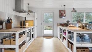 Une cuisine moderne avec des meubles blancs, un plan de travail en bois et une vue sur l’extérieur grâce à une grande fenêtre.