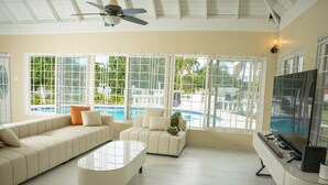 A spacious living room with a large sofa, a coffee table, and a TV stand with a flat-screen TV. - Newly Renovated!! COCO PALMS - Exclusive villa with private pool/beach access.  (Mammee Bay, Mammee Bay Estates)