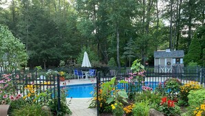 A backyard with a swimming pool, surrounded by a fence, and featuring a patio area with chairs and a table. - Saratoga retreat!  Great yard with inground pool.  4 miles from Racetrack. (Saratoga Springs)