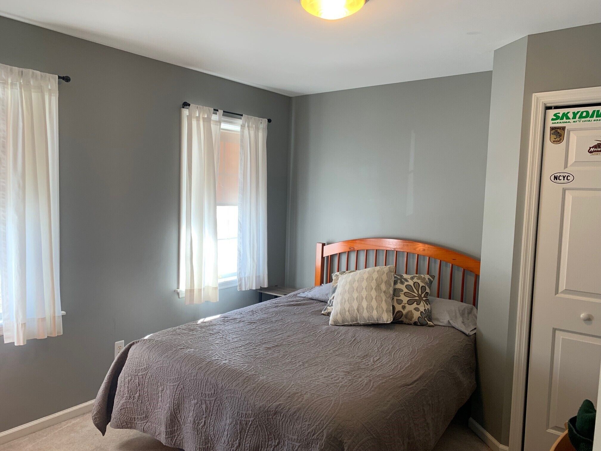Un dormitorio con cama, ventana con cortinas y puerta con un adhesivo.
