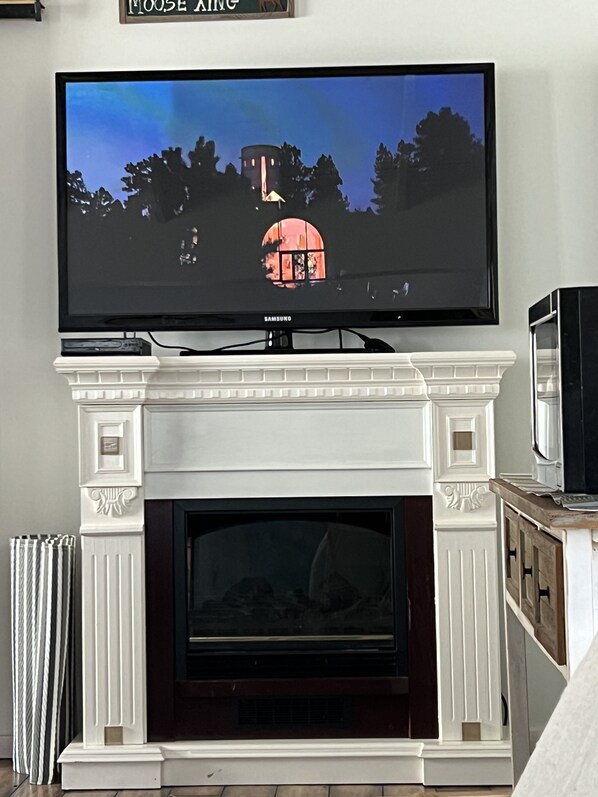 Een flatscreen televisie bevestigd boven een witte schoorsteenmantel met een open haard eronder.
