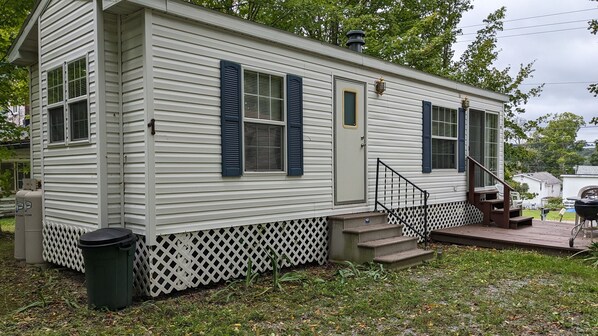 A single-story mobile home with a front porch, a small set of steps, and a trash can.