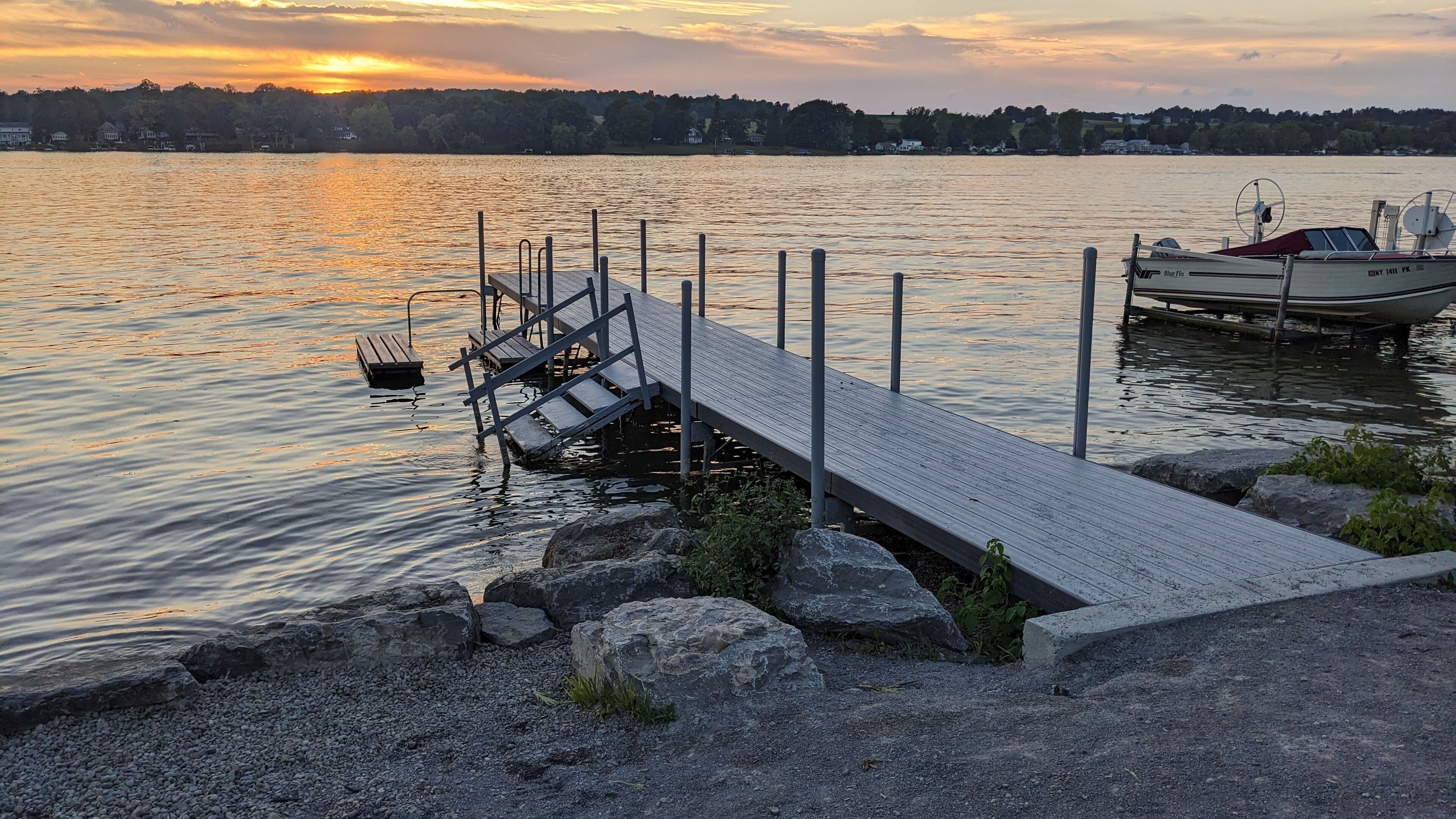 A wooden dock extending into calm water with a boat docked on the right.