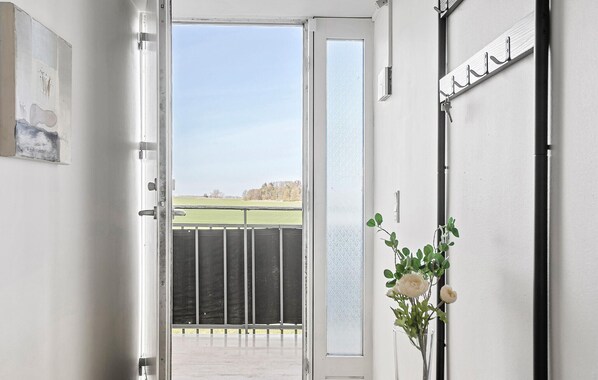 Puerta abierta que da a un balcón con vistas a un campo verde y árboles.