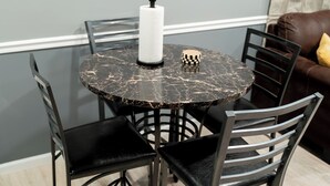 A round dining table with four chairs, a white bottle, and a black and white checkered object on the table. - JC Entire Apartment remodeled, close to Airport and Ferry (Coram)