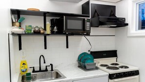 A kitchen with a white countertop, a stainless steel sink, a black microwave, a stove, and a dish rack. - JC Entire Apartment remodeled, close to Airport and Ferry (Coram)