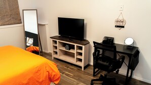 A bedroom with a bed, a TV on a wooden stand, a desk with a chair, and a wall-mounted light. - JC Entire Apartment remodeled, close to Airport and Ferry (Coram)