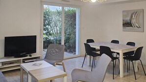 A modern living room with a flat-screen TV, a dining table with chairs, and a sofa. - 2 bedroom amazing apartment in Le Pellerin (Le Pellerin)