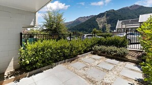Ein Innenhof mit einem Steinweg, einem schwarzen Metallzaun und einem Berg im Hintergrund.