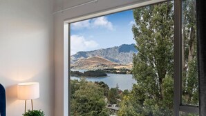 Ein Zimmer mit großem Fenster und Blick auf einen See, Berge und Bäume.