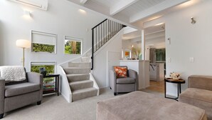 Una sala de estar moderna con una escalera, sofás grises y una cocina al fondo.