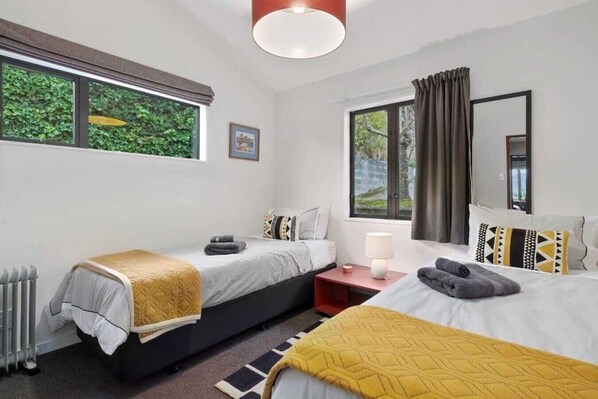 A modern hotel room with two single beds, a bedside table with a lamp, a window with curtains, and a radiator. - 5 minute walk into town, carpark and views of lake and mountains (Queenstown)