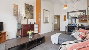 Ein modernes Wohnzimmer mit einer Couch, einem Couchtisch und einem Fernseher. Ein Bücherregal mit Dekorationselementen und eine Tür zu einem anderen Raum.