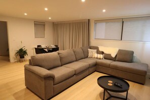 A modern living room with a sectional sofa, a small round table, and a dining area in the background. - 5 minute easy walk to Queenstown, warm and spacious. (Queenstown)