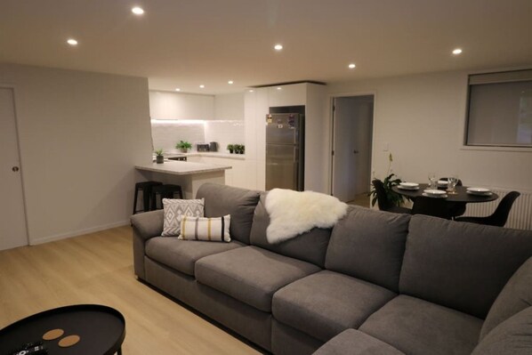 A modern living room with a grey sofa, a small black table, and a kitchen area in the background. - 5 minute easy walk to Queenstown, warm and spacious. (Queenstown)