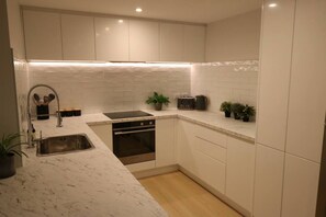 A modern kitchen with white cabinets, a stainless steel sink, a built-in oven, and a countertop with a toaster and potted plants. - 5 minute easy walk to Queenstown, warm and spacious. (Queenstown)