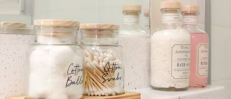 A bathroom shelf with jars of cotton balls, cotton swabs, and bath salts.