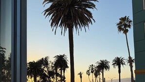 A view of a street lined with palm trees and parked cars, with a building in the foreground and a body of water in the background. - Santa Monica Ocean View Suite (Santa Monica)