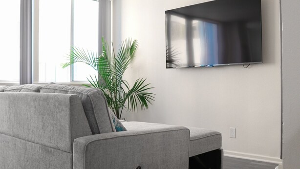 A modern living room with a grey sofa, large windows, a flat-screen TV, and a potted plant. - Santa Monica Ocean View Suite (Santa Monica)