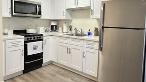A modern kitchen with white cabinets, a stainless steel refrigerator, a microwave, a stove, and a coffee maker. - Santa Monica Ocean View Suite (Santa Monica)