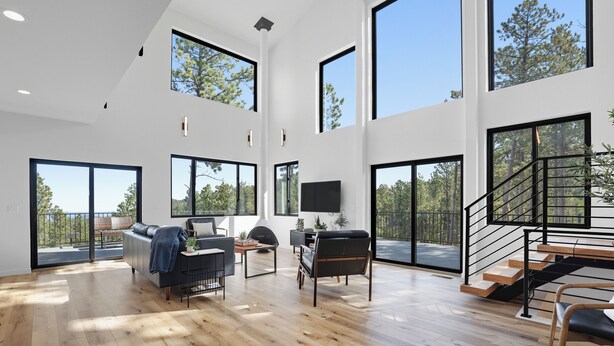 A spacious living area with large windows, a staircase, and a flat-screen TV. - The Falcon- Breathtaking Mountain Views (Rapid City)