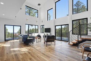 A spacious living area with large windows, a staircase, and a flat-screen TV. - The Falcon- Breathtaking Mountain Views (Rapid City)
