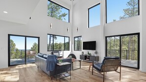 A spacious living room with a large sofa, a coffee table, and a fireplace. There are large windows providing natural light and views of the outdoors. - The Falcon- Breathtaking Mountain Views (Rapid City)