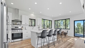 A modern kitchen with white cabinetry, a stainless steel stove, and a large island with bar stools. - The Falcon- Breathtaking Mountain Views (Rapid City)