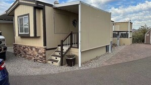 Ein eingeschossiges Gebäude mit heller Fassade, einem Hauseingang mit Treppe und einem kleinen Außenbereich mit Blumentopf.
