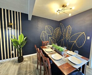 A dining area with a dark blue wall, a wooden dining table set with plates and glasses, and a potted plant. -  Updated, Spacious, Convenient Location  (Bedford)