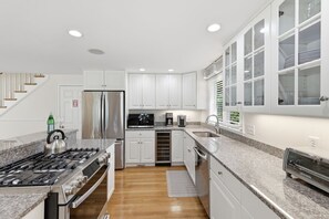 A modern kitchen with white cabinetry, a stainless steel refrigerator, a built-in oven, and a granite countertop.
