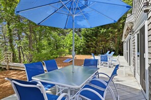 An outdoor patio with a table and chairs, a blue umbrella, and a wooden deck.