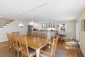 A spacious dining area with a wooden table and chairs, a kitchen in the background, and a staircase leading upstairs.