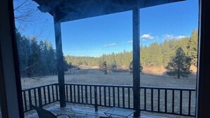 Un espace extérieur abrité, équipé de deux chaises et d’une table, qui offre une vue sur un paysage boisé.