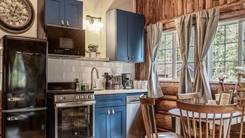 A kitchen with blue cabinets, a black refrigerator, a stove, and a dining area with a wooden table and chairs.