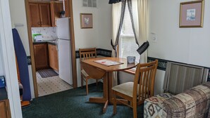 A compact kitchen with wooden cabinets, a white refrigerator, and a dining table with chairs. - Park model unit #2 for rent by Silver Lake NY  (Perry)