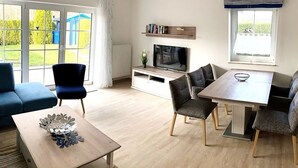 Moderni olohuone, jossa on sohva, sohvapöytä, televisio sekä ruokailutila, jossa on tuoleja ja pöytä.