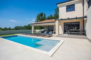 Una casa moderna con piscina, mobiliario de exterior y un patio cubierto.