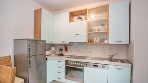 Een compacte keuken met lichtblauwe kastjes, een roestvrijstalen koelkast, een oven en een vaatwasser.