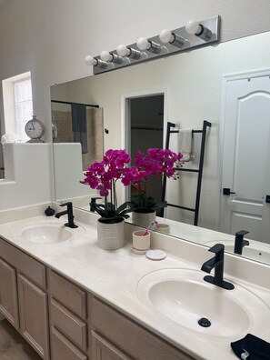A bathroom with two sinks, a mirror, a clock, and a potted orchid.