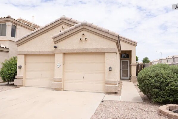 A single-story house with a beige facade, a garage, and a small front yard with a bush.