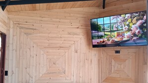 A cozy room with a wooden ceiling, a teal sofa with two cushions, and a television displaying a floral scene. - Glamping Caelum, Refugio al Aire Libre. Macheta Cundinamarca (Machetá)