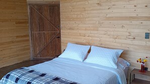 A wooden cabin bedroom with a bed, a wooden door, and a nightstand with a vase. - Glamping Caelum, Refugio al Aire Libre. Macheta Cundinamarca (Machetá)