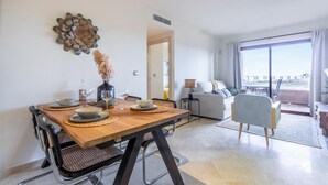 A modern living room with a dining area. There is a wooden dining table with chairs, a sofa, and a view of the outdoors through large windows. - Amazing apartment in Los Alcázares (Los Alcázares)